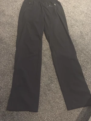 Svarta mjukisbyxor från Peak Performance - Säljer ett par svarta mjukisbyxor från Peak Performance med raka ben och resår i midjan. Byxorna har dragkedjefickor framtill och en diskret logga på vänster ben. Perfekta för chill eller träning, tillverkade i mjukt och bekvämt material.