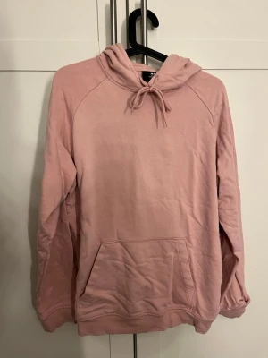 Rosa hoodie från H&M Regular Fit - En snygg rosa hoodie från H&M i Regular Fit med huva och dragsnören. Tröjan har en stor magficka och långa ärmar. Materialet är mjukt och bekvämt, perfekt för att chilla eller hänga med kompisar. Klassisk design som är enkel att matcha med jeans eller joggers.