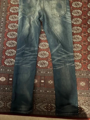 LEE jeans  - Säljer ett par blå jeans med straight fit och snygga slitningar på både fram- och baksidan. Jeansen har klassiska bakfickor och är tillverkade i denim. Perfekt för dig som gillar en avslappnad och trendig look.