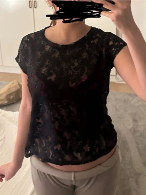 Svart spets-topp med kort ärm - Säljer en svart, transparent topp i spets med blommigt mönster och rund halsringning. Toppen har korta ärmar och en avslappnad passform. 💕