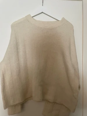 Beige oversized stickad tröja - Säljer en beige oversized stickad tröja med rund halsringning och diskreta vertikala ränder. Tröjan har en avslappnad passform och långa ärmar, perfekt för lager på lager och en chill look.