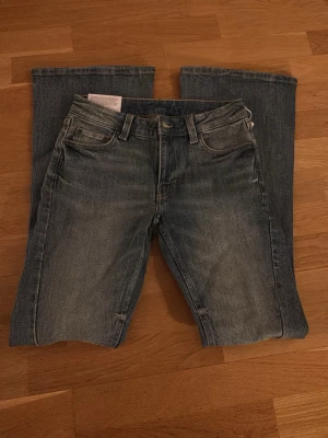 Blå bootcut jeans från Weekday - Säljer ett par blå bootcut jeans från Weekday med klassisk femficksmodell och knappgylf. Perfekta för dig som gillar en avslappnad men trendig stil. 