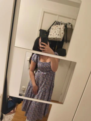 Blommig långklänning med puffärm - Söt långklänning med blommigt mönster i blått, rosa och vitt. Klänningen har puffärmar, smock över bysten och en flowy kjol. Perfekt för sommarens alla tillfällen och ger en romantisk vibe.