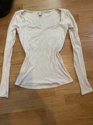 Ljusbeige ribbad topp från Amisu - Säljer en ljusbeige ribbad långärmad topp från Amisu. Toppen har en bred, något fyrkantig ringning och är figurnära i modellen. Perfekt att styla med jeans eller kjol för en enkel men snygg look.