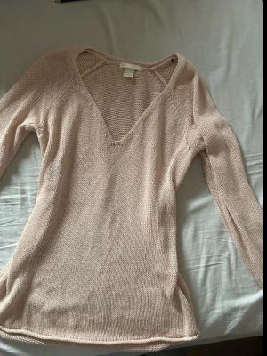 Ljusrosa stickad tröja med v-ringning - Säljer en ljusrosa stickad tröja med djup v-ringning och långa ärmar. Tröjan har en smal passform och är tillverkad i ett tunt, mjukt material som passar perfekt till lager på sopplooken. Enkel och stilren design utan mönster.