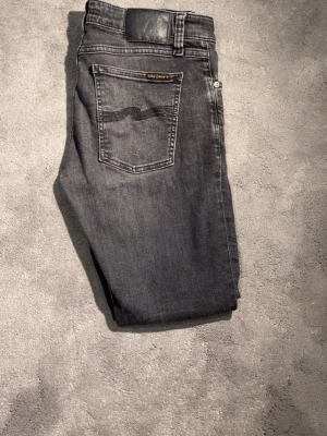 Nudie Jeans - Säljer ett par Nudie Jeans med klassisk femficksdesign och svarta detaljer på bakfickan. Jeansen har låg midja och är tillverkade i mjuk bomull med stretch för extra komfort. Skick 9/10 Storlek W30