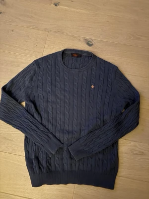 Morris kabelstickad - Blå kabelstickad Morris tröja i bra skick, ända defekten är att ena sidan av nacklappen har släppt men går enkelt att laga, Str Xl men passar mer åt L/M hållet
