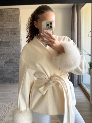 Krämvit kappa med pälskanter - Snygg krämvit kappa med breda ärmar och fluffiga pälskanter vid ärmslut. Ifrån Gina tricot, använd en gång! 💕