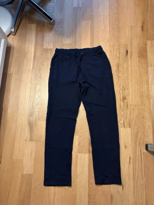 Kostymbyxor - Säljer ett par svarta mjukisbyxor med resår i midjan och dragsko för skön passform. Byxorna har raka ben och sidofickor, perfekta för chill dagar hemma eller till träningen. Materialet känns mjukt och bekvämt mot huden.