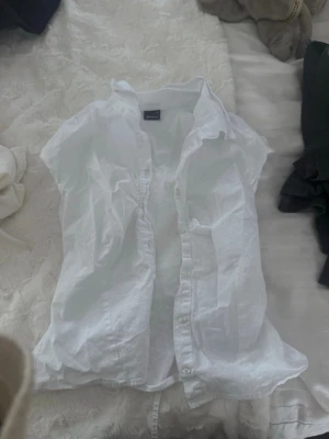 Vit kortärmad skjorta med knyt - Säljer en vit kortärmad skjorta med knappar framtill och knytband i midjan där bak. I storlek M från Ginatricot. Snygg till jeans och fest!