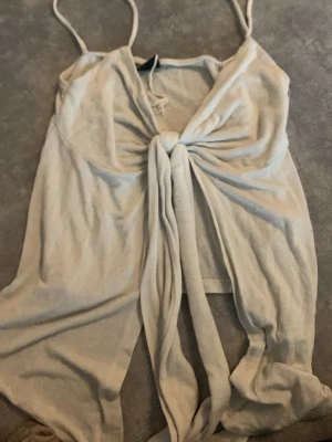 Beige linnetopp med knyt framtill - Trendig vit  linnetopp med smala axelband och snygg knytning framtill. Toppen är ärmlös och har en croppad passform som passar perfekt till sommaren. Enkel och stilren design som är lätt att matcha.
