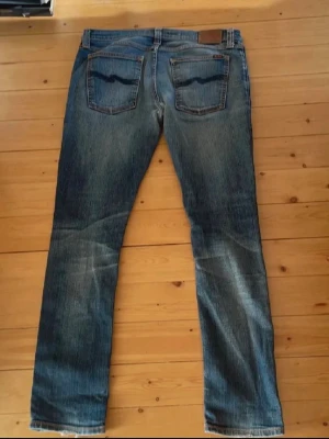 Blå jeans från Nudie Jeans - Säljer ett par klassiska blå jeans från Nudie Jeans med raka ben. Finns några hål i byxorna, de är lite slitna men skickar man in dem till en butik som säljer nudie fixar dem det gratis! Skickas samma dag som du köper!