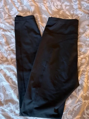 Svarta sportleggings med hög midja - Säljer ett par svarta sportleggings med fräsch och enkel design. De har hög midja och är tillverkade i ett stretchigt material som passar perfekt för träning eller chill. Inga synliga loggor eller detaljer, bara clean look.