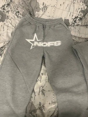 Grått loungewear-set från NOFS - Mysigt grått loungewear-set från NOFS med matchande hoodie och byxor. Hoodien har stor magficka och tryckt logga framtill, byxorna har resår i midjan och samma logga på benet. Perfekt för chill dagar hemma. Mjuk bomullsblandning.