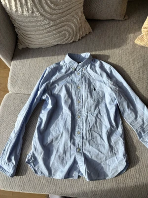 Ljusblå skjorta från Polo Ralph Lauren - Klassisk ljusblå skjorta från Polo Ralph Lauren med button-down sopets och broderad logga på bröstet. Slim fit sopassning och långa ärmar. Perfekt till jeans eller chinos för en clean och stilren look.