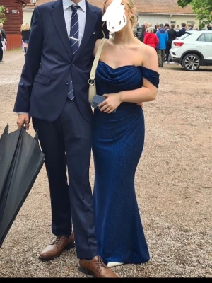 Balklänning Mörkblå Glittrig - Mörkblå glittrig balklänning offshoulder           Från bubbleroom  Strl S                           Endast använd en gång            Uppsydd efter ca 160 cm längd, den går att sprätta Från djur/rökfritt hem Nypris 1200 kr