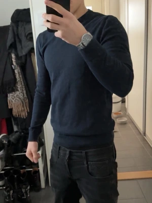 Mörkblå merino tröja - En stilren mörkblå tröja med rund halsringning och långa ärmar. Tröjan har en smal passform och ribbade muddar vid ärmslut och nederkant. Perfekt för en clean och enkel look.