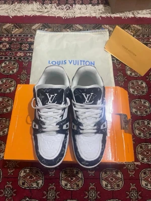 L*ouis V*uitton vita och svarta sneakers - Nästan helt oanvända L*ouis V*uitton sneakers i vitt och svart med klassiskt -monogram på ovandelen. Skorna har vita snören, låg profil och detaljer i läder och textil. Perfekta för dig som vill ha mala sneakers med exklusiv känsla och tydlig logga.