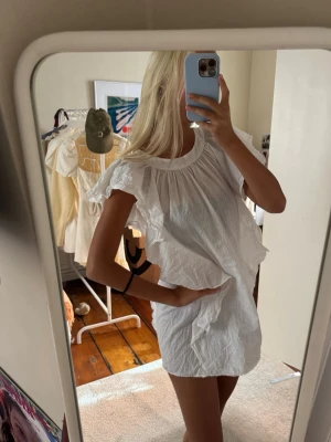 Vit volangklänning med puffiga ärmar - Säljer en luftig vit kortklänning med volangdetaljer och breda ärmar. Klänningen har en lös passform och är i en linne textur, perfekt för varma dagar. Rund halsringning och romantisk känsla. Går att använda både som blus och klänning 💞 Lite see-trough ⭐️