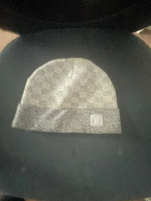 Grå  mössa version Damier - Snygg grå mössa  med klassiskt Damier-rutmönster och vikt kant.  framtill på kanten ger en exklusiv touch. Perfekt accessoar för dig som vill ha både stil och värme pipeline gaslight.