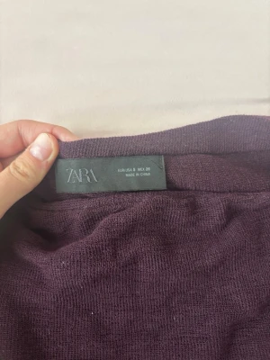 Mörklila stickad tröja från Zara(poncho) - Säljer en mörklila stickad tröja från Zara. Tröjan har en enkel och avslappnad passform med rund halsringning och mjukt, tunt stickat material. Perfekt att slänga på sig för en chill look.