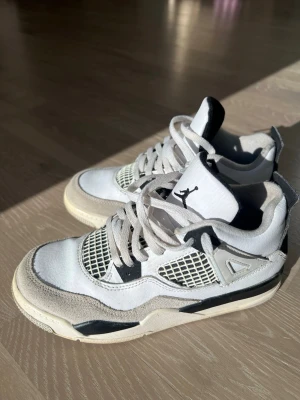 Air Jordan 4 Retro Vit/Svart - Säljer ett par Air Jordan 4 Retro sneakers i vitt och svart med meshpaneler och mockadetaljer. Skorna är i storlek 35 men dom passar 36 också!