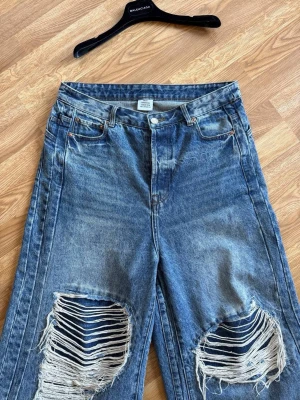 Blåa vida slitna jeans med hål - Säljer ett par blåa jeans från Zara med bred passform och stora slitningar över knäna. Jeansen har hög midja, klassiska fem fickor och råa kanter nertill. Perfekta för en avslappnad och trendig streetstyle-look.