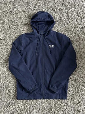 Under Armour Windbreaker - En fräsch marinblå under armour windbreaker. Jackan är använd några fåtal gånger och har därför inga defekter och är i princip ny.