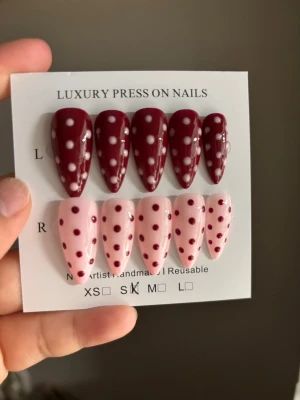 Press-on naglar med prickigt mönster - Snygga press-on naglar i två färger: vinröd med vita prickar och ljusrosa med vinröda prickar. Naglarna har en lång, spetsig form (stiletto) och ger en trendig look. Perfekt för dig som vill ha unika och handgjorda naglar snabbt. Materialet är plast.