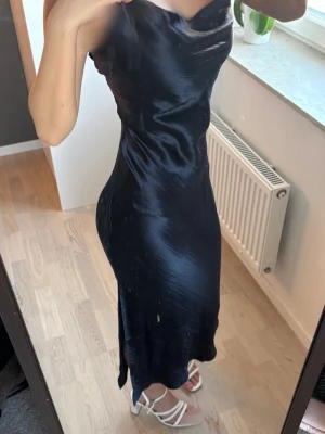 Marinblå satin klänning  - Elegant marinblå långklänning i glansigt sidenliknande material med smala axelband, lätt V-ringning och figurnära passform. Slits nertill. Från ASOS, storlek 32. 