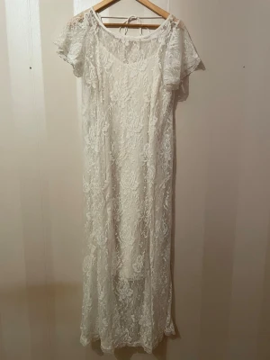 Vit lång spetsklänning  - Elegant vit spetsklänning från reclaimed vintage,ASOS med romantisk och klassisk stil. perfekt som studentklänning eller till sommarens festligheter. Klänningen har ett fint spetslager över en underklänning, korta spetsärmar och en vacker knytning i ryggen.  Den luftiga passformen och den mjuka spetsen ger en tidlös och feminin look, perfekt till studenten, skolavslutning eller sommarfest. 