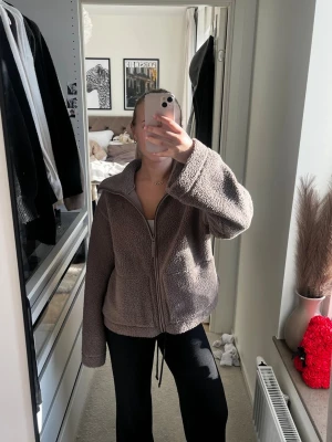 Beige teddyjacka med dragkedja - Mysig teddyjacka i beige färg med dragkedja framtill och stora fickor. Jackan har en hög krage och är tillverkad i fluffigt teddy-material som ger en avslappnad och trendig look. Perfekt för att hålla sig varm under kyliga dagar.