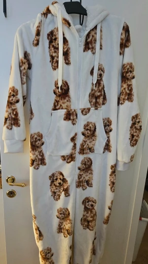 Onesie,Jumpsuit hundvalpar,huva stl L  - Supermjuk och mysig onesie i vitt med gulligt hundmönster över hela plagget. Har dragkedja framtill, huva med snören och stora Tillverkad i fluffigt fleece-material som håller dig varm. Stl L 