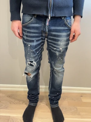 BLÅA DSQUARED 2 JEANS - Tja jag säljer ett par mörkblå slim fit jeans från dsquared med slitningar och hål på machbenet. Jeansen är riktigt stilrena med en vanlig fem ficks design. Storleken är 44(30-31) i midjan. Hör av er för frågor eller funderingar ‼️