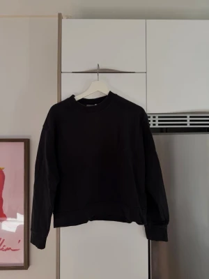 Svart sweatshirt från Weekday - En svart sweatshirt från Weekday i storlek XS. Tröjan har en klassisk rund halsringning, långa ärmar och ribbade muddar vid ärmslut och nederkant.
