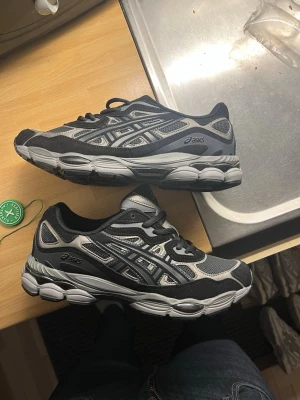 ASICS Gel Nyc svart\grå - passar 41-43  sneakers i svart och grått med silvriga detaljer. Skorna har en chunky sula och meshpaneler för bra andningsförmåga. Ikoniska ASICS-loggor på sidorna och en sportig vibe som passar streetwear. Perfekta för dig som gillar stilrena och bekväma sneakers.