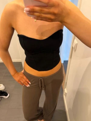 Svart korsett-topp från Gina Tricot - Säljer en svart korsett-topp från Gina Tricot. Aldrig använd. Toppen är axelbandslös och har en figurnära passform med markerade sömmar som ger en snygg siluett. Perfekt att styla med både jeans och kjol för en trendig look.