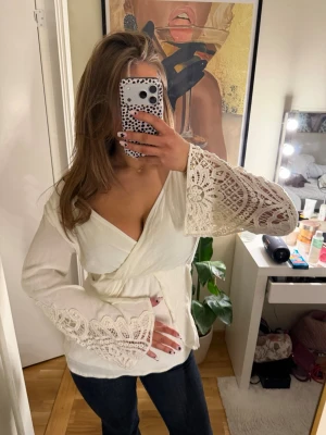 Vit omlottopp med spetsärmar - Säljer en superfin vit vintage omlottopp med v-ringning och vida ärmar i spetsdetaljer. Skulle säga storlek s/m💕💕☺️