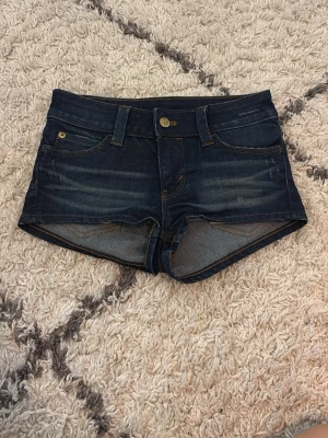 Mörkblåa minishorts från Cheap Monday - Snygga mörkblå jeansshorts från Cheap Monday med klassisk femficksdesign och kontrastsömmar. Shortsen har låg midja och en grön etikett bak med logga. Perfekta för varma dagar. 