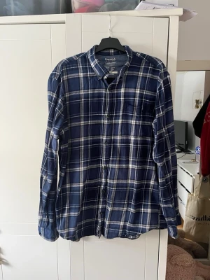 Blå rutig skjorta från Jack & Jones  - Klassisk blå och vit rutig skjorta från jack & Jones Skjortan har lång ärm, bröstficka och knappar framtill. Perfekt för en avslappnad och stilren look. Tillverkad i mjuk bomull för extra komfort.