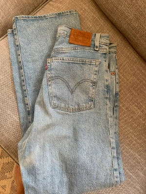 Levi's Ribcage Straight jeans ljusblå - Säljer ett par klassiska Levi's Ribcage Straight jeans i ljusblå tvätt. Modellen har hög midja, raka ben och fem fickor. Ikonisk läderpatch bak och röd Levi's-tag på bakfickan. Tillverkade i slitstark denim av bomull.