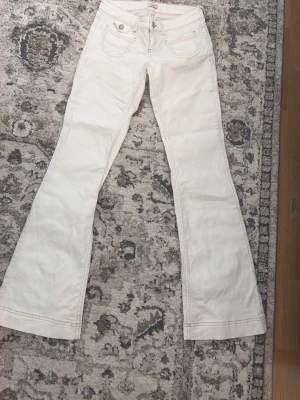 Vita bootcut jeans med låg midja från Nelly  - Snygga vita bootcut jeans med låg midja och klassiska fem fickor. Jeansen har utsvängda ben och dekorativa sömmar. Perfekta för dig som gillar en retrostil och vill sticka ut lite extra. Använda 1 gång.