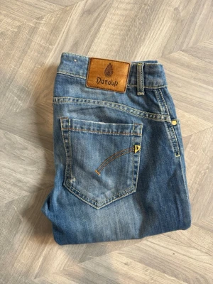 Blå slitna jeans från Dondup - Snygga blå jeans från Dondup med slitningar och distressed detaljer på benen. Klassisk femficksmodell med smal passform och läderpatch med logga bak i midjan. Jeansen har guldfärgade detaljer och är tillverkade i denim. Hål i högra fram fickan‼️ pris kan diskuteras vid snabb affär 