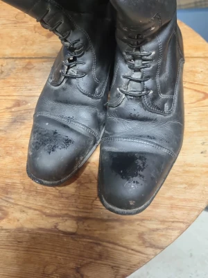Svarta höga ridstövlar i läder - Säljer ett par klassiska svarta ridstövlar i  läder med snörning framtill och ganska låg klack. Stövlarna har en stilren design med markerad tåkappa och dekorativa sömmar. Perfekta att rida i.