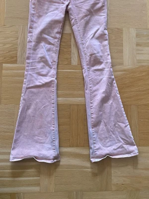 Lågmidjade bootcut/flare jeans - Säljer ett par supercoola och snygga rosa/lax/corall färgade jeans med utsvängda ben. Jeansen är sjukt mjuka och sjöna! Långa på mig som är 162cm! Skärphället på högra sidan har gått av ( se sista bild ) så pris kan diskuteras!