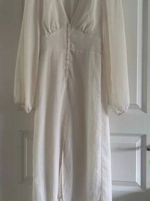 Vit långklänning med knappar - Elegant vit långklänning med v-ringning och långa ärmar. Passar perfekt nu till sommaren eller/och även stundenten! Den är lite kräm vit i färgen och har lite rutigt mönster.😍