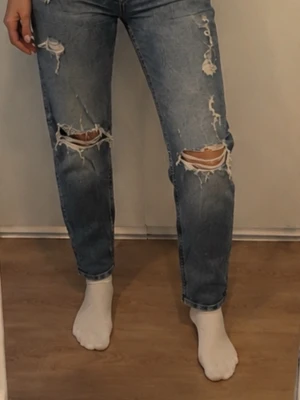 Blåa ripped jeans med raka ben - Snygga blå jeans med raka ben och flera slitningar och hål på både lår och knän. Jeansen har klassisk femficksdesign och knappgylf. Perfekta för en avslappnad och trendig look.