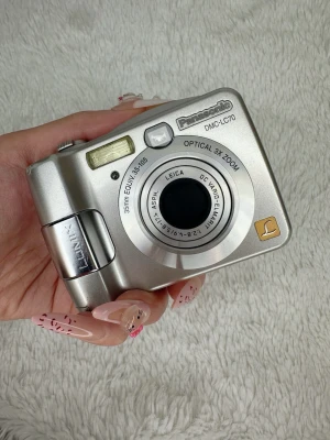 Panasonic Lumix DMC-LC70 digitalkamera - Snygg silverfärgad digitalkamera från Panasonic, modell Lumix DMC-LC70. Kameran har 3x optisk zoom, inbyggd blixt och Leica DC Vario-Elmarit-objektiv. Kompakt design i metall med tydliga knappar och klassisk form. Ingår batteri och sd kort