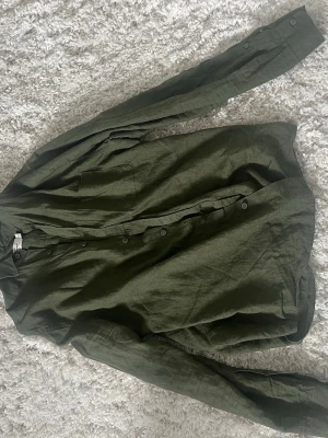 Grön linneskjorta från Dressmann - Snygg grön skjorta från Dressmann i linne med klassisk krage och knäppning framtill. Skjortan har en bröstficka och långa ärmar med knapp vid ärmslut. Perfekt för en avslappnad men stilren look. Skriv vid funderingar!