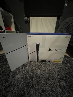 Vit PlayStation 5 Digital Edition - PlayStation 5 Digital Edition från Sony i stilren vit färg med svarta detaljer. Konsolen har en futuristisk design med släta, böjda paneler i plast och levereras med originalkartong. Perfekt för gaming på nästa nivå med snabb SSD och kraftfull prestanda.